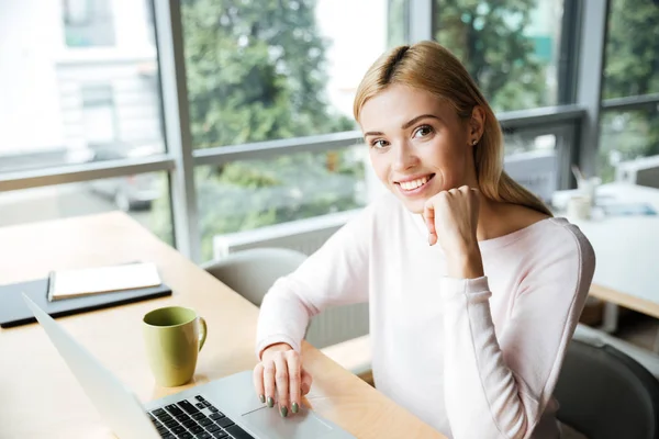 Веселая женщина, сидящая в офисе и работающая с ноутбуком — стоковое фото