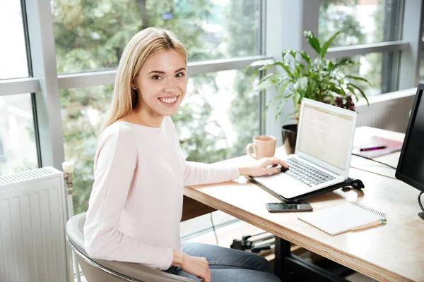 Senhora alegre sentado no escritório coworking usando laptop — Fotografia de Stock