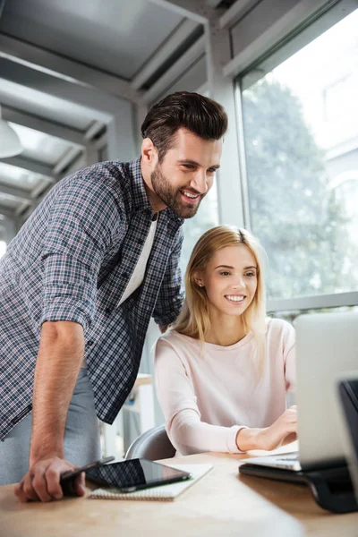 Smiling two colleagues in office coworking while using laptop — Stock Photo, Image