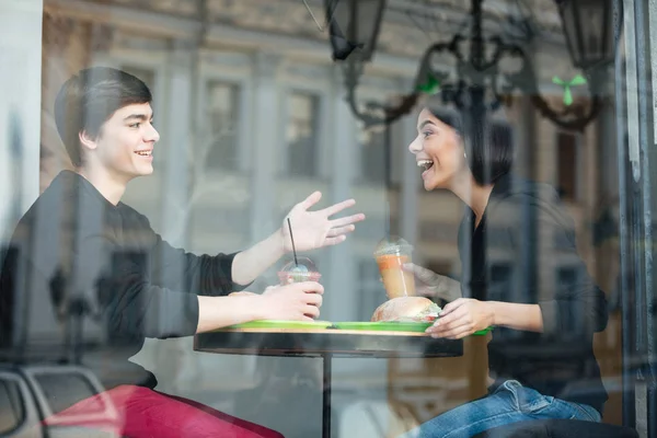 Jovem sorridente sentado no café com sua irmã bebendo suco — Fotografia de Stock