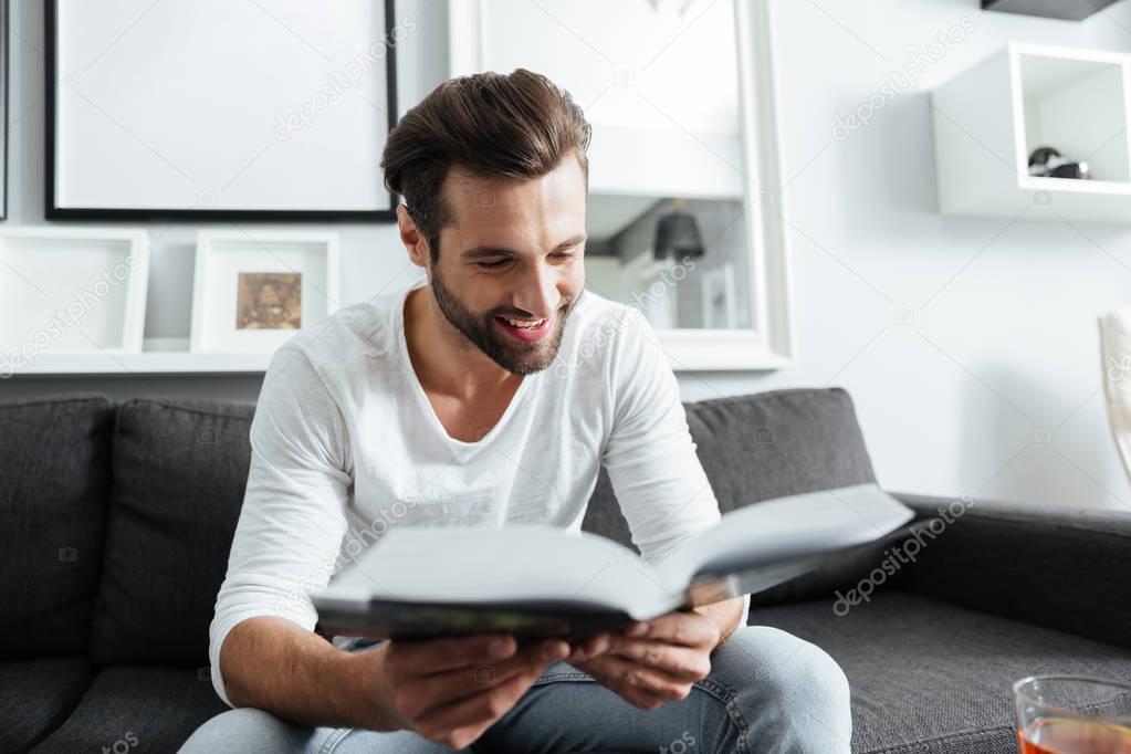 Cheerful man sitting on sofa reading book
