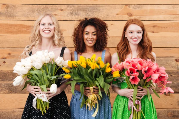 Três mulheres sorridentes mostrando buquês de flores na câmera — Fotografia de Stock