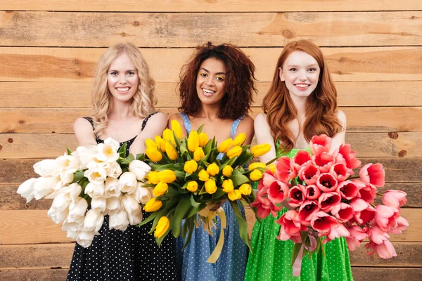 Tre donne sorridenti che mostrano mazzi di fiori alla macchina fotografica — Foto Stock