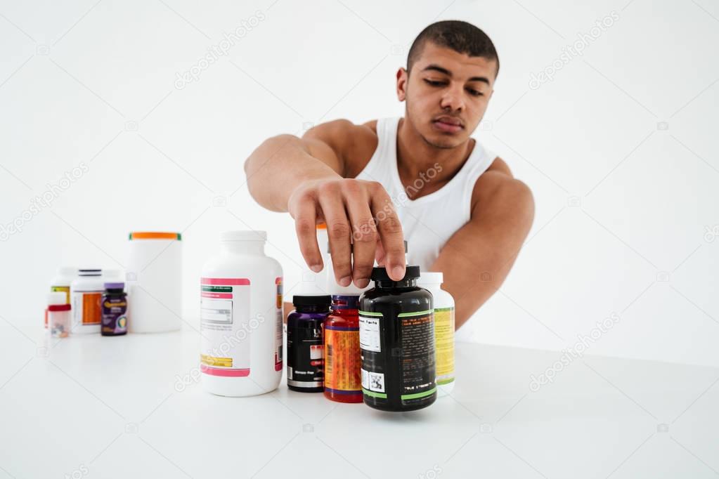 Sportsman standing over white background holding vitamins