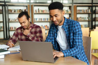 Genç gülümseyen Afrika erkek öğrenci dizüstü bilgisayar için bir çalışma kullanarak