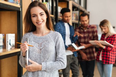 Defter tutan kitaplığında ayakta mutlu kadın öğrenci