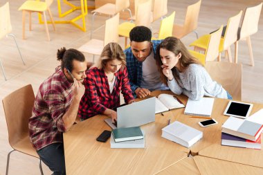 Konsantre öğrenciler dizüstü bilgisayar kullanan kitaplığında oturan.