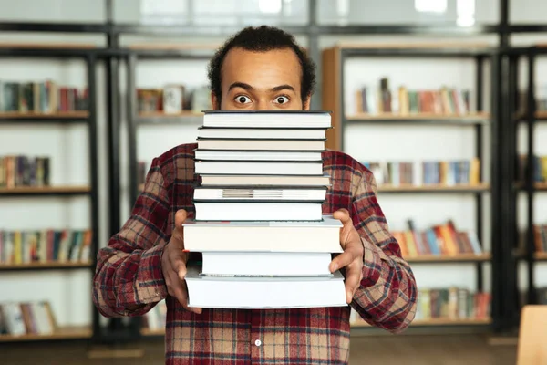 Geschokt Afrikaanse man student permanent in bibliotheek met boeken — Stockfoto