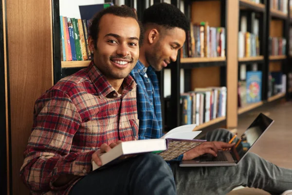 Jovem feliz dois homens africanos estudantes sentados na biblioteca — Fotografia de Stock