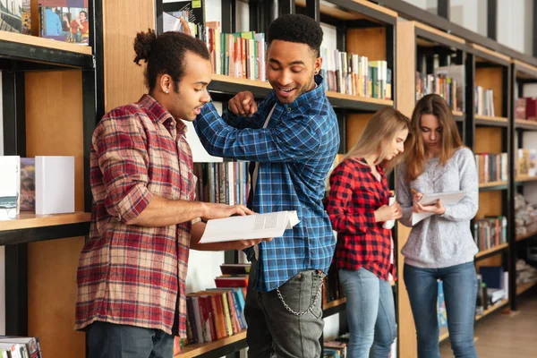 Jóvenes hombres serios estudiantes de pie en la biblioteca leyendo libros —  Fotos de Stock