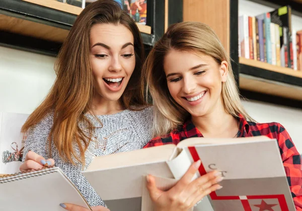 Twee vrouwelijke studenten lezen van boeken in de bibliotheek te glimlachen — Stockfoto