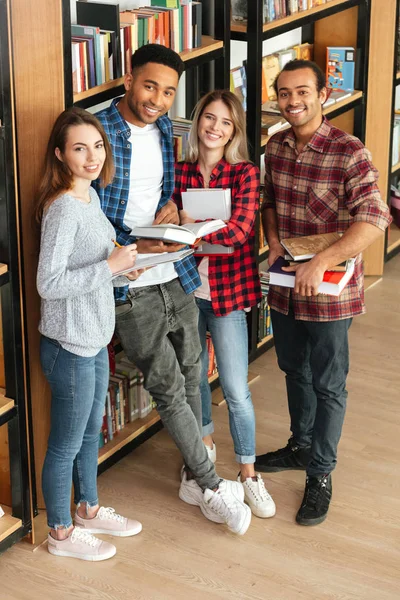 Estudiantes felices de pie en biblioteca leyendo libro — Foto de Stock