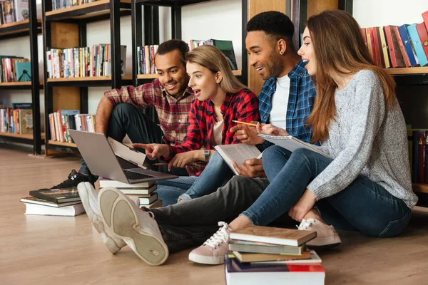 Koncentruje studentów siedzi w bibliotece na podłodze przy użyciu laptopa — Zdjęcie stockowe