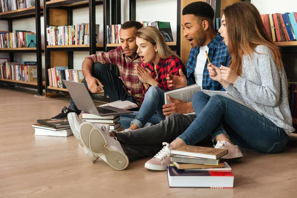 Концентровані студенти сидять у бібліотеці на підлозі за допомогою ноутбука — стокове фото