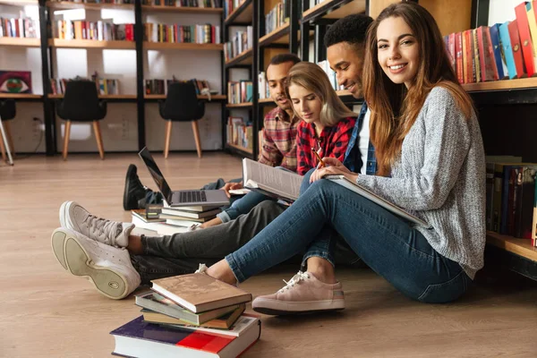 Geconcentreerd studenten zitten in bibliotheek op vloer met behulp van laptop — Stockfoto