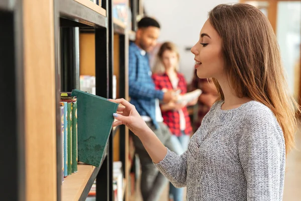 Νέοι όμορφο φοιτητή γυναίκα στέκεται στη βιβλιοθήκη, κρατώντας το βιβλίο. — Φωτογραφία Αρχείου