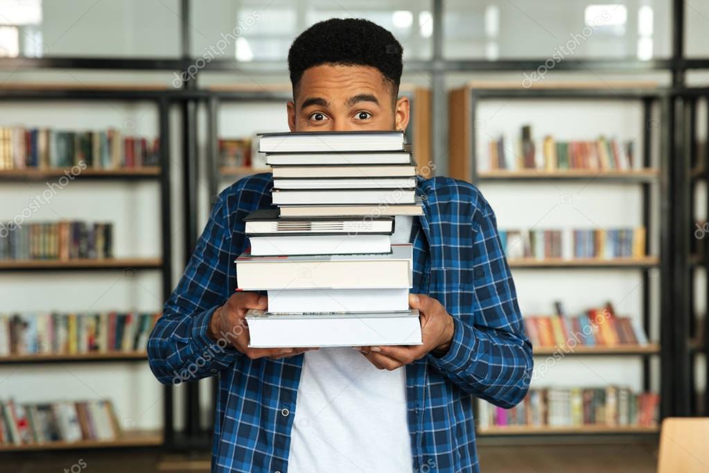 Young afro american male student holding stack of books