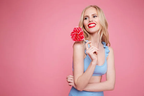 Retrato de una hermosa mujer rubia sonriente en traje de baño posando con piruleta en forma de corazón y mirando hacia otro lado — Foto de Stock