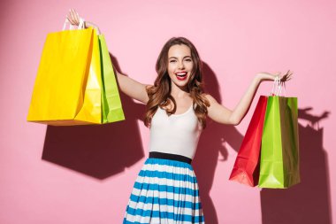 Mutlu kız pembe arka plan üzerinde izole renkli alışveriş çantaları taşırken