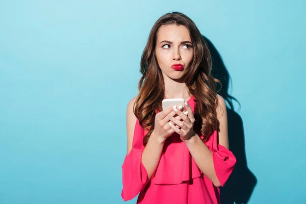 Porträtt av en förvirrad tjej i klänning som håller mobiltelefon — Stockfoto