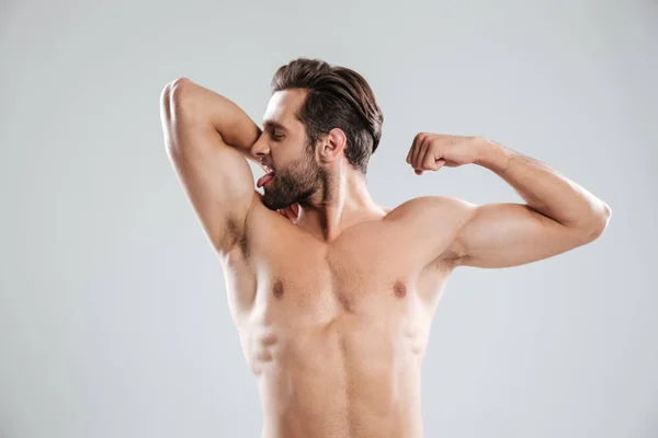 Handsome young naked man showing and kissing his biceps — Stock Photo, Image