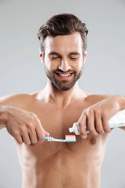 Retrato de un hombre sonriente poniendo pasta de dientes en un cepillo de dientes —  Fotos de Stock