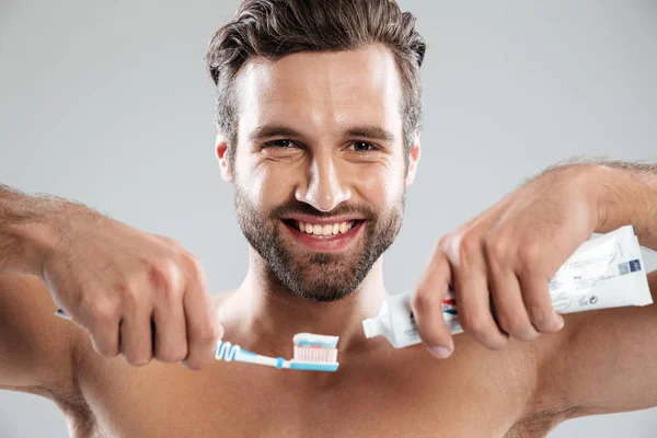 Retrato de un hombre sonriente poniendo pasta de dientes en un cepillo de dientes —  Fotos de Stock