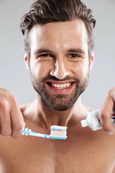 Retrato de un hombre sonriente poniendo pasta de dientes en un cepillo de dientes — Foto de Stock