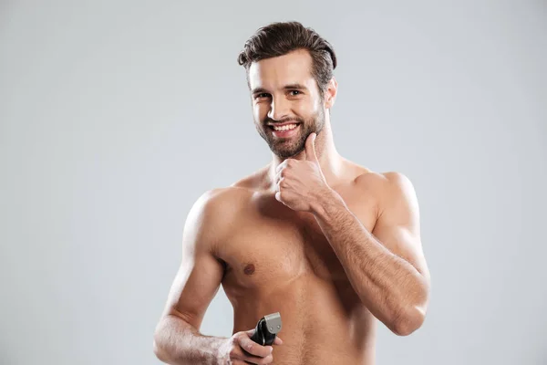 Pohledný mladý muž, držící elektrický holicí strojek a dojemné bradu — Stock fotografie