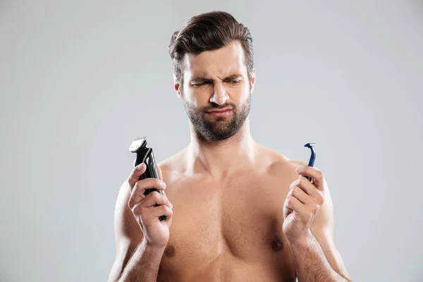 Portrait of a doubtful young man choosing razor — Stock Photo, Image