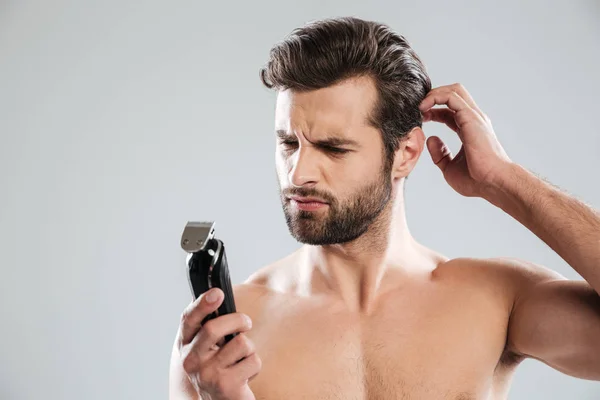 Портрет бородатого чоловіка, який дивиться на електричну бритву — стокове фото