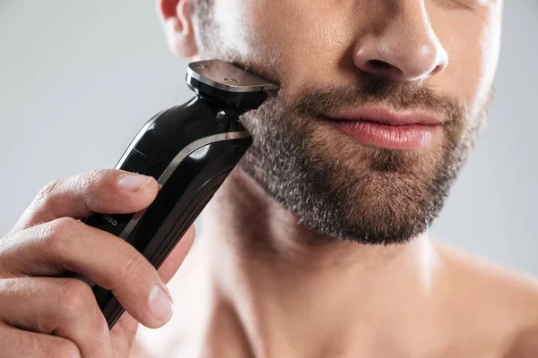 Обрезанное изображение бородатого человека с помощью электрической бритвы — стоковое фото