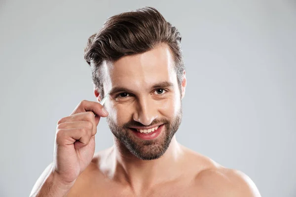 Beau jeune homme pincant ses sourcils avec une pince à épiler — Photo