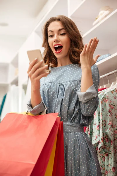 Lykkelig kvinne med smarttelefon og pakker som står i butikk stockbilde