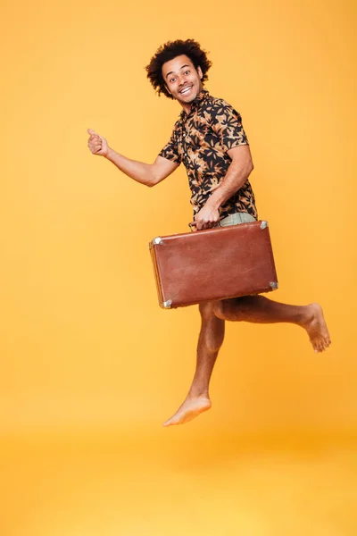 Glada afrikanska mannen hoppa innehav resväska och visar tummen upp. — Stockfoto