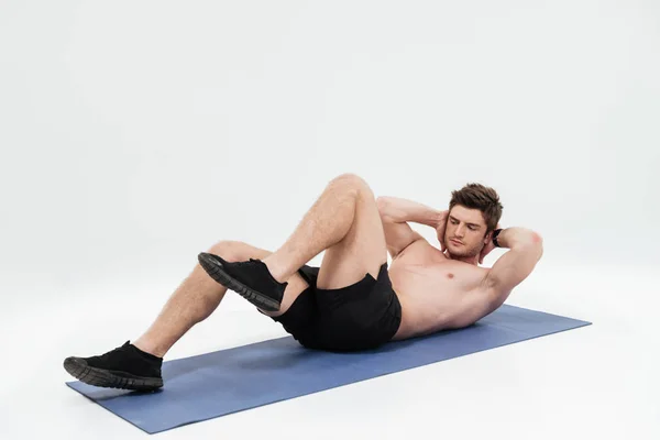 Joven deportista guapo haciendo ejercicios de piernas en una alfombra de fitness — Foto de Stock