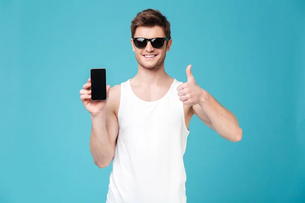 Joven mostrando la pantalla en blanco del teléfono inteligente annd gesto — Foto de Stock