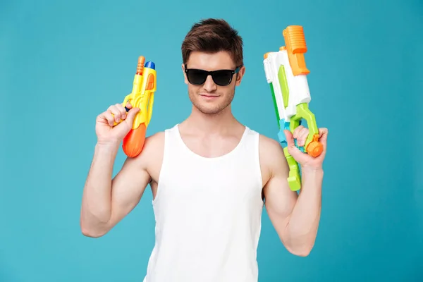 Positive man looking camera and holding two water guns — Stock Photo, Image