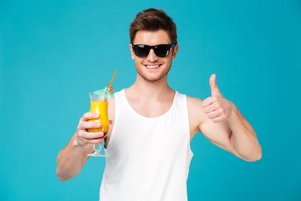 Hombre joven en gafas de sol mostrando cóctel y pulgar hacia arriba — Foto de Stock