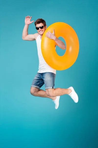 Feliz hombre excitado en gafas de sol sosteniendo anillo inflable y saltando — Foto de Stock