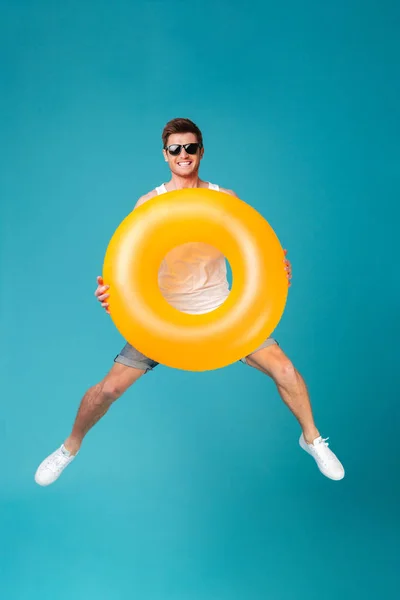 Glücklich aufgeregter Mann mit Sonnenbrille hält aufblasbaren Ring und springt — Stockfoto