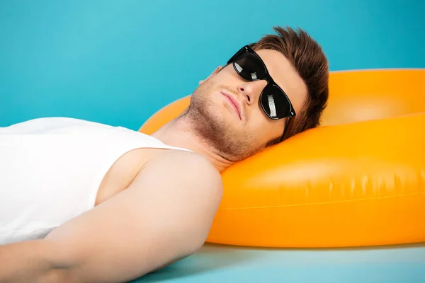 Pohledný mladý muž v sluneční brýle relaxační na nafukovací kruh — Stock fotografie