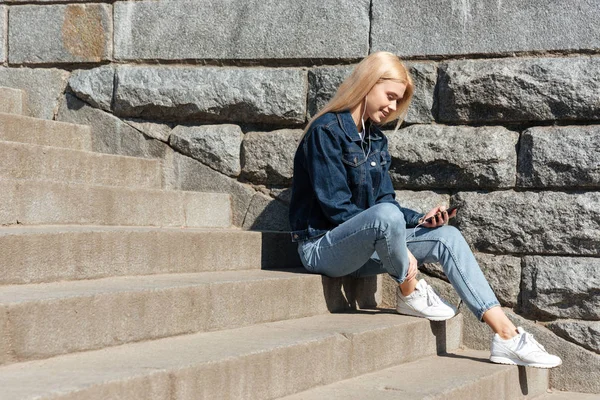 Blondi nainen käyttää smarthone ja kuulokkeet — kuvapankkivalokuva
