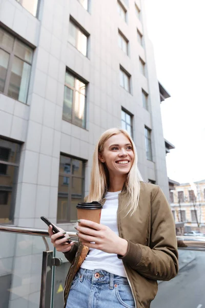 Veselá žena s šálkem kávy a smartphone dívá stranou — Stock fotografie