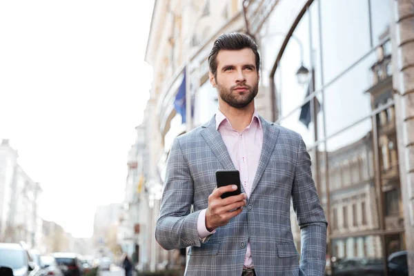 Красивый мужчина в куртке ходит и держит в руках мобильный телефон — стоковое фото