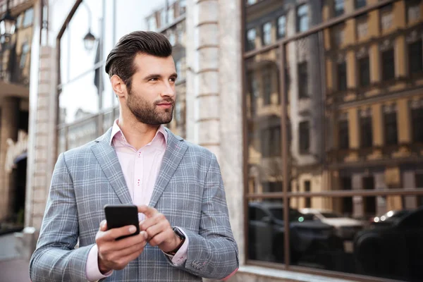 Красивый мужчина в куртке стоит и держит в руках мобильный телефон — стоковое фото