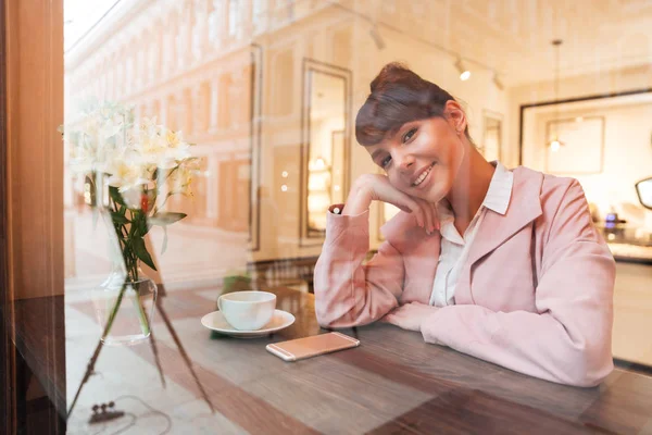 Uśmiechający się ładna dziewczyna siedzi przy stole café w pomieszczeniu — Zdjęcie stockowe