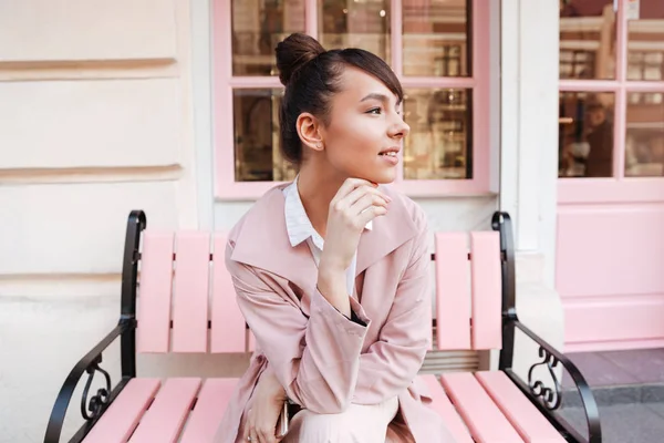 Chica sonriente en abrigo rosa relajándose en el banco al aire libre —  Fotos de Stock