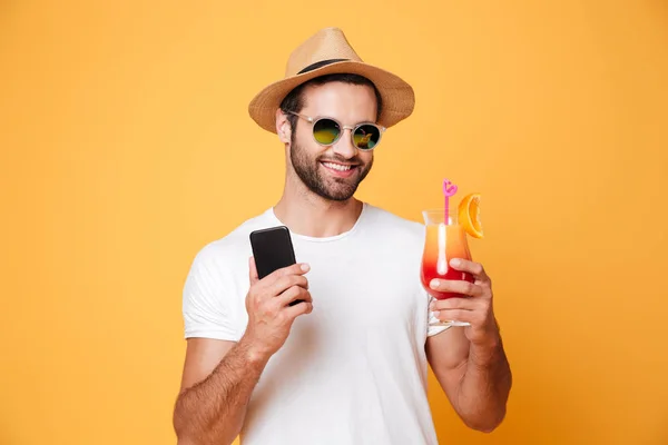 Feliz joven sosteniendo el teléfono móvil y cóctel . — Foto de Stock