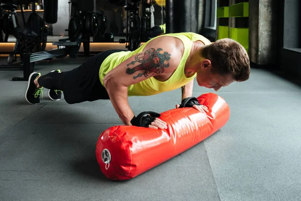 Joven deportista fuerte haciendo flexiones y usando saco de boxeo — Foto de Stock